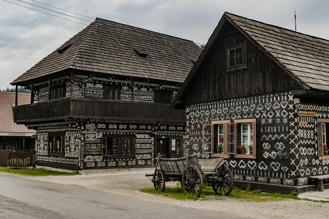Tradičné čičmianske zrubové drevenice s bielymi maľovanými ornamentmi a šindľovou strechou, pred nimi drevený voz