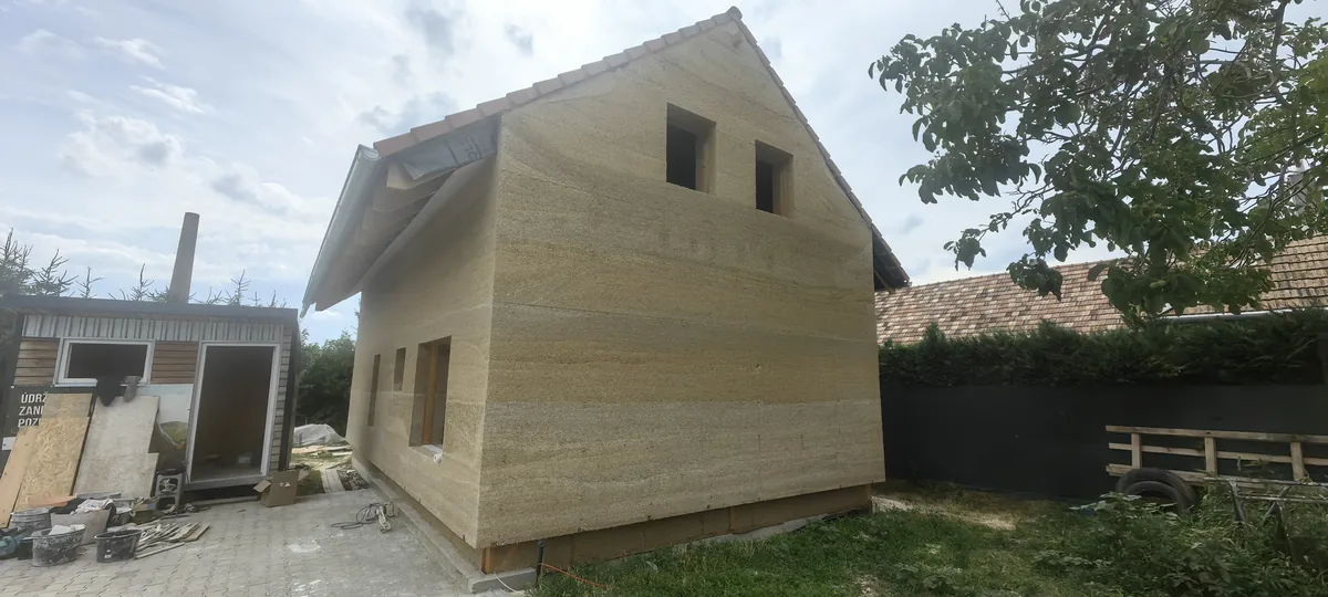 Rozostavaný rodinný dom v Šali s obvodovou stenou z konopného betónu hrúbky 400 mm pred omietaním, na stene sú viditeľné vodorovné vrstvy po debnení, strecha s pálenou krytinou je hotová, otvory okien zatiaľ prázdne