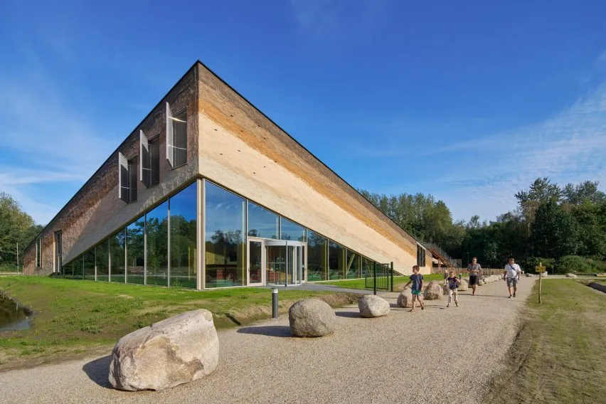 Museumpark Vonk v Eindhovene: šikmá fasáda z vrstveného konopného betónu so zasklenou prízemnou časťou a návštevníkmi pred vchodom